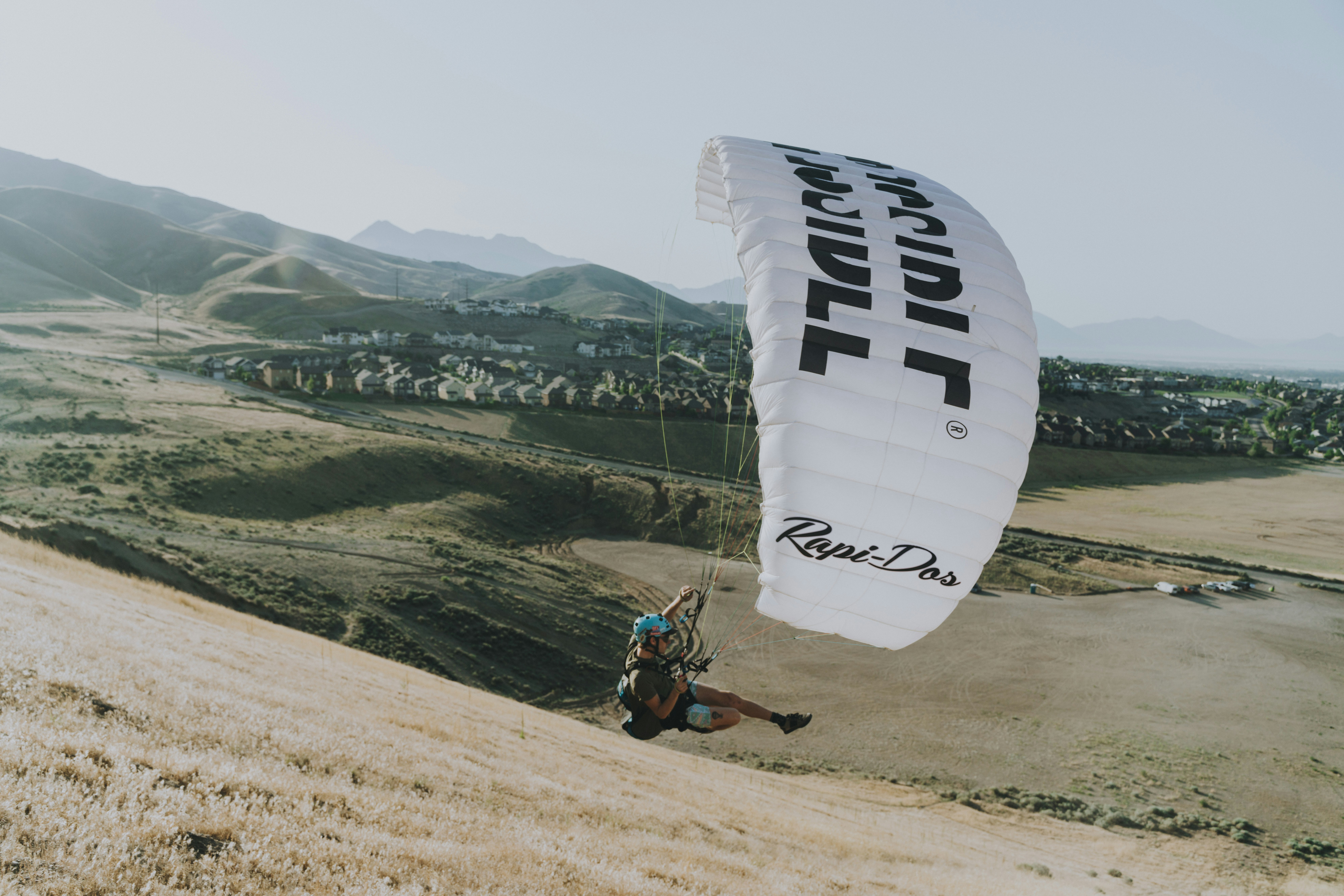 man riding on red and white parachute over green mountains during daytime
